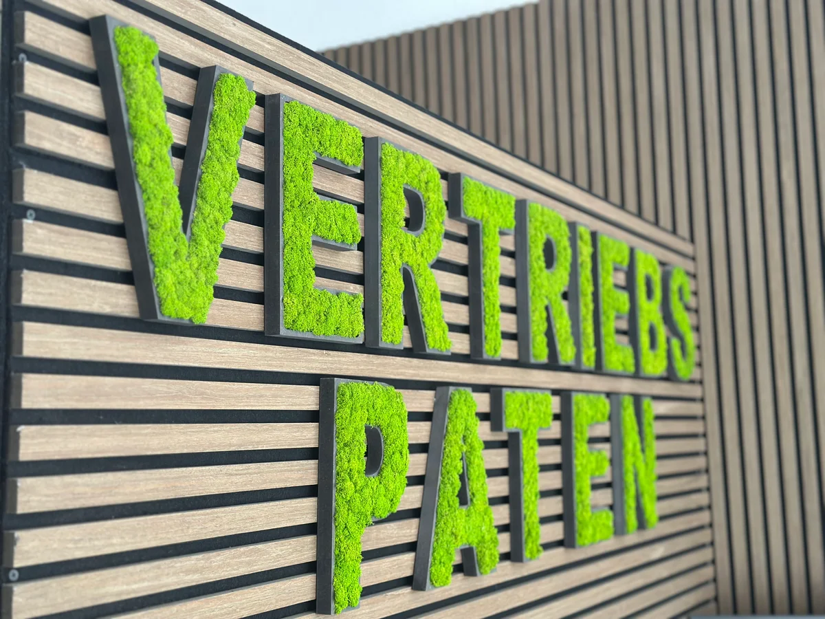 Grüner VertriebsPaten-Schriftzug an der Holzwand im Büro der Vertriebsagentur